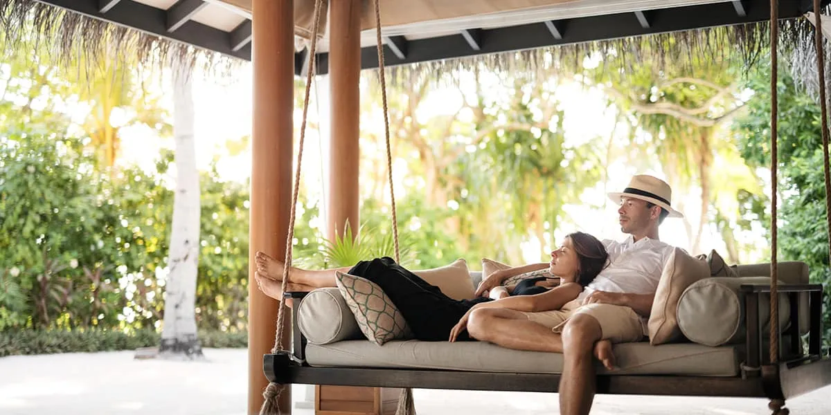 Couple relaxing on a hanging swing daybed under a thatched pavilion