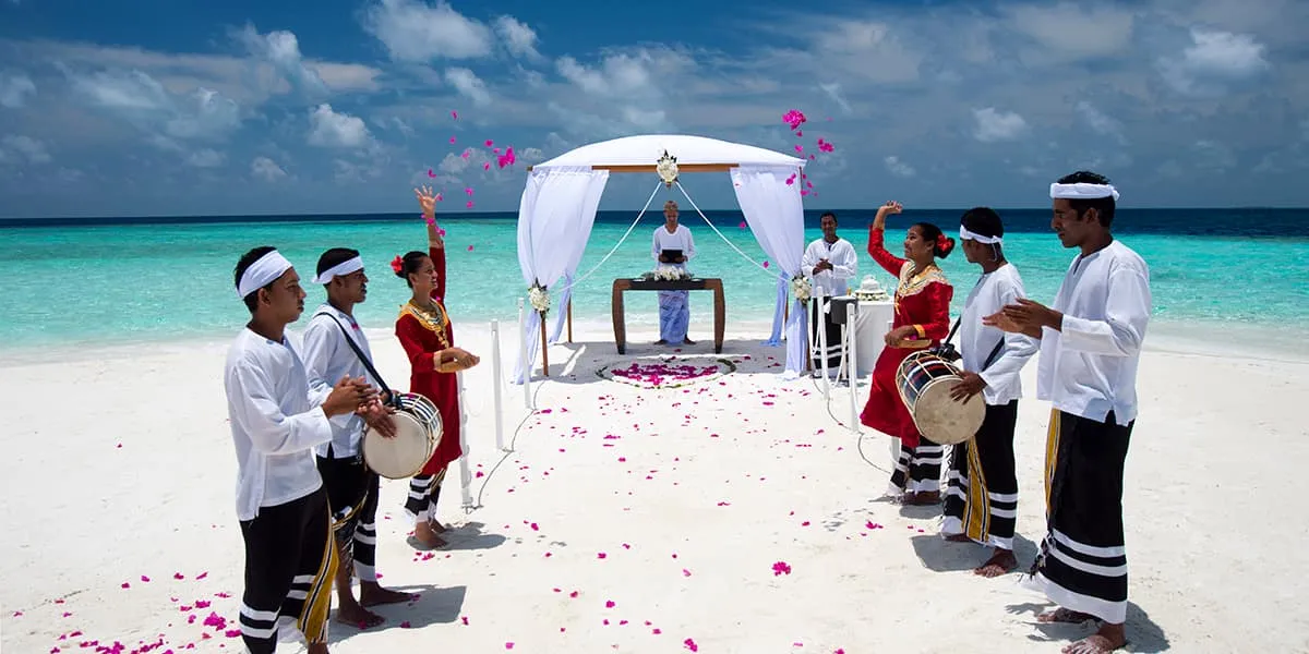Drummers in white performing at a beach wedding with a flower-strewn aisle