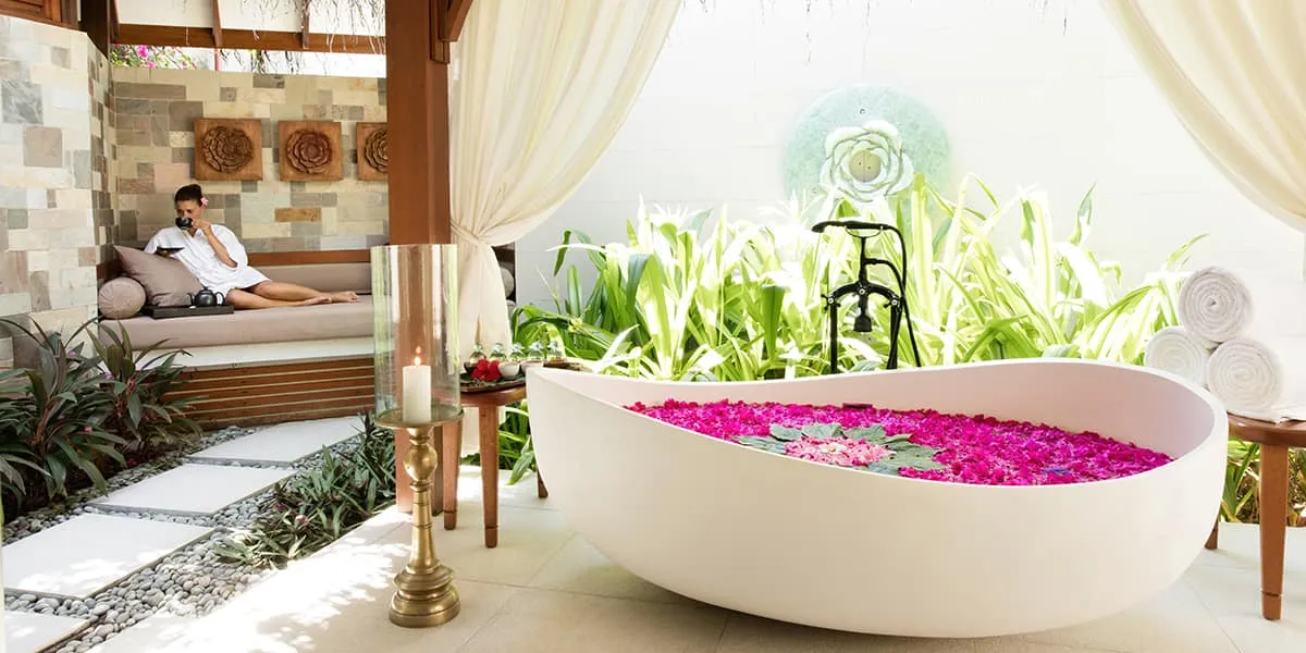 Petal-filled freestanding bath in an open-air spa garden, guest resting behind