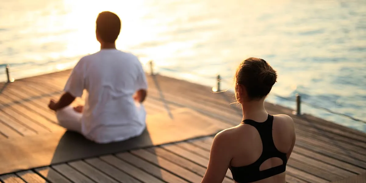 Two guests practising sunrise yoga on a wooden deck by the sea