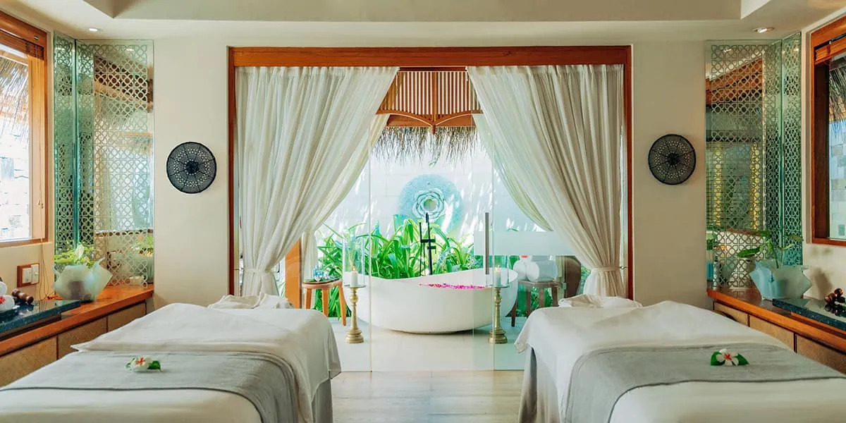 Spa suite with two treatment beds and a flower bath beyond white curtains