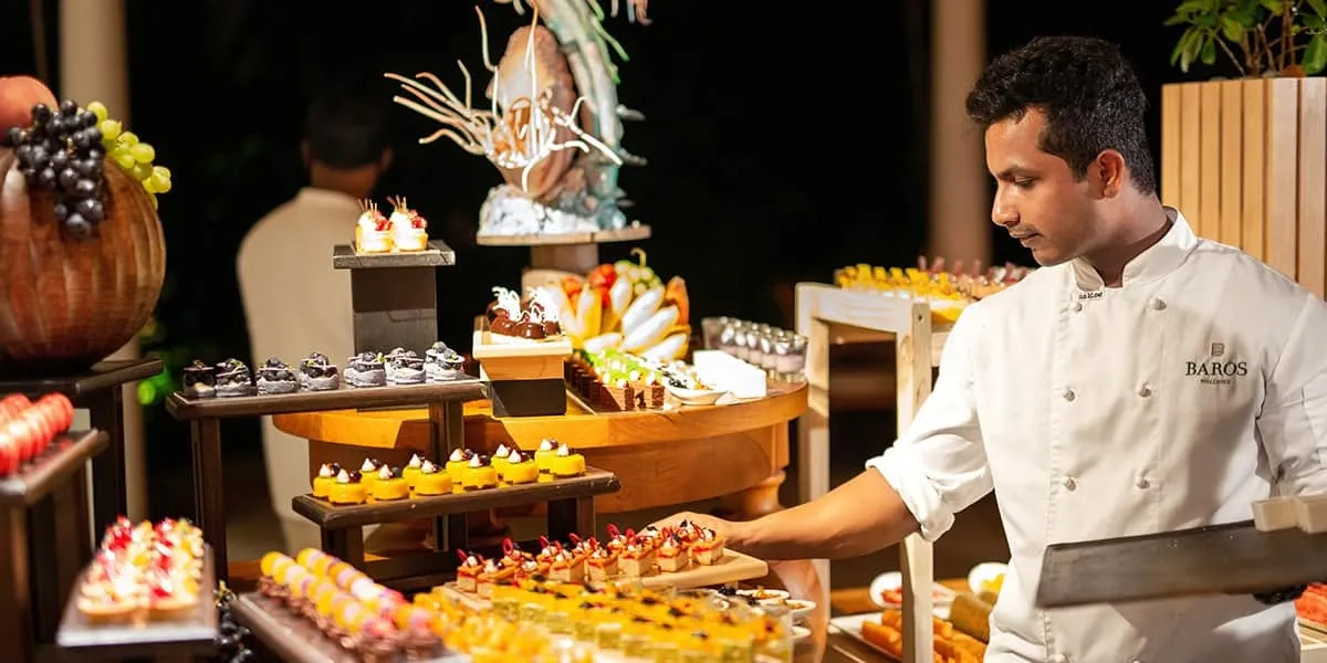 Chef in whites beside a festive dessert buffet at night
