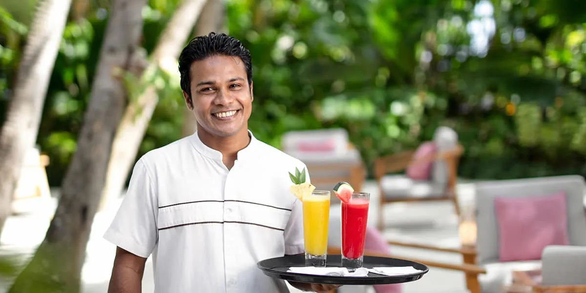 Smiling waiter holding a tray of fresh fruit juices in a garden