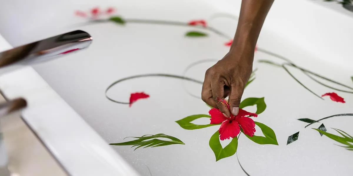 Hand arranging red flowers and green leaves into a pattern on a white bed
