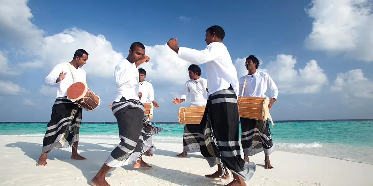 Bodu beru drummers in white shirts and sarongs performing on a sandbank