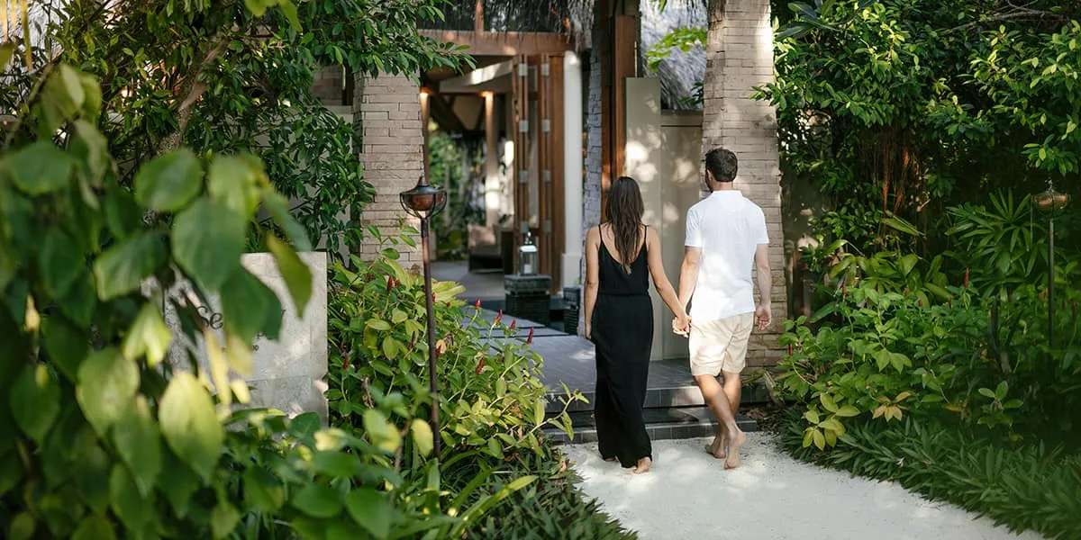 Couple walking hand in hand along a garden path between villas