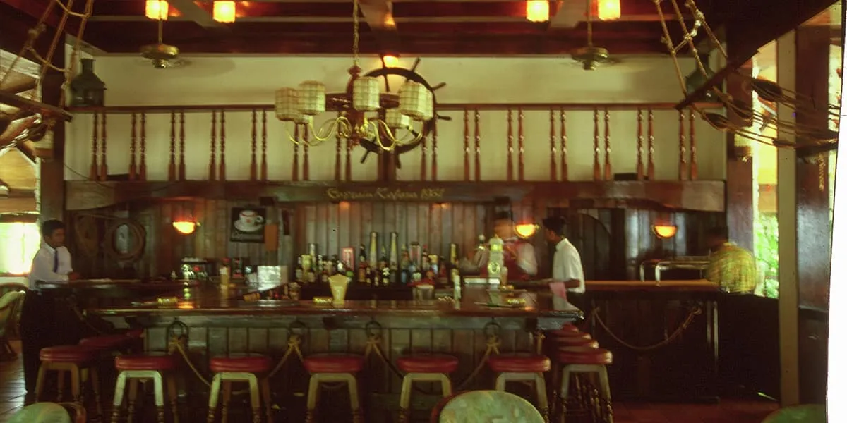Wood-panelled bar with stools and a ship's wheel above the counter