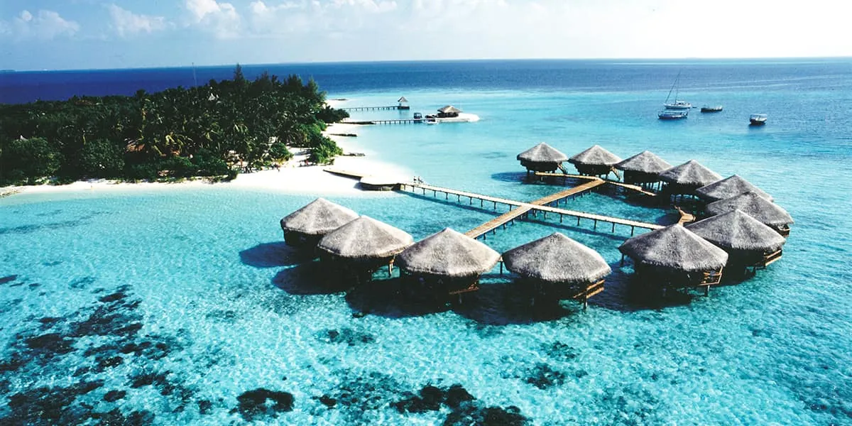 Early aerial view of Baros island with thatched water villas on the lagoon