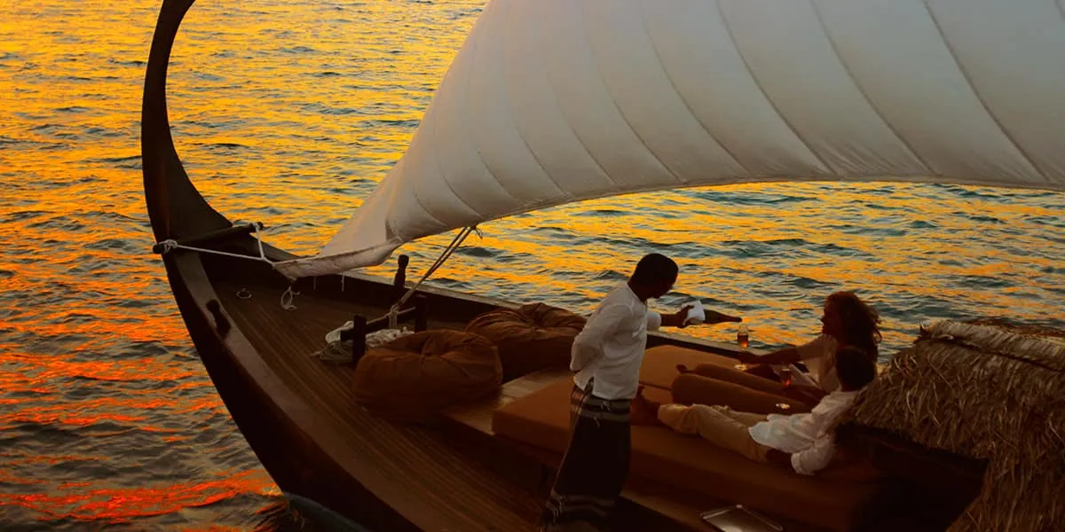 Crew member serving a couple aboard a sailing dhoni at sunset