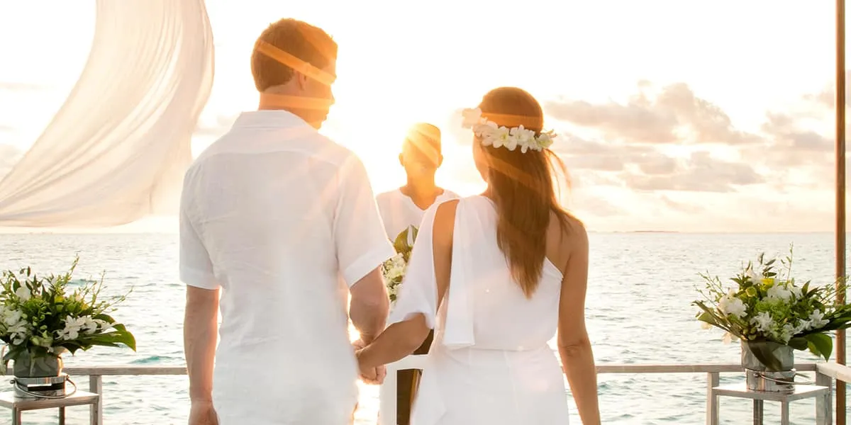 Couple in white holding hands on a deck by the sea, bride with a flower crown