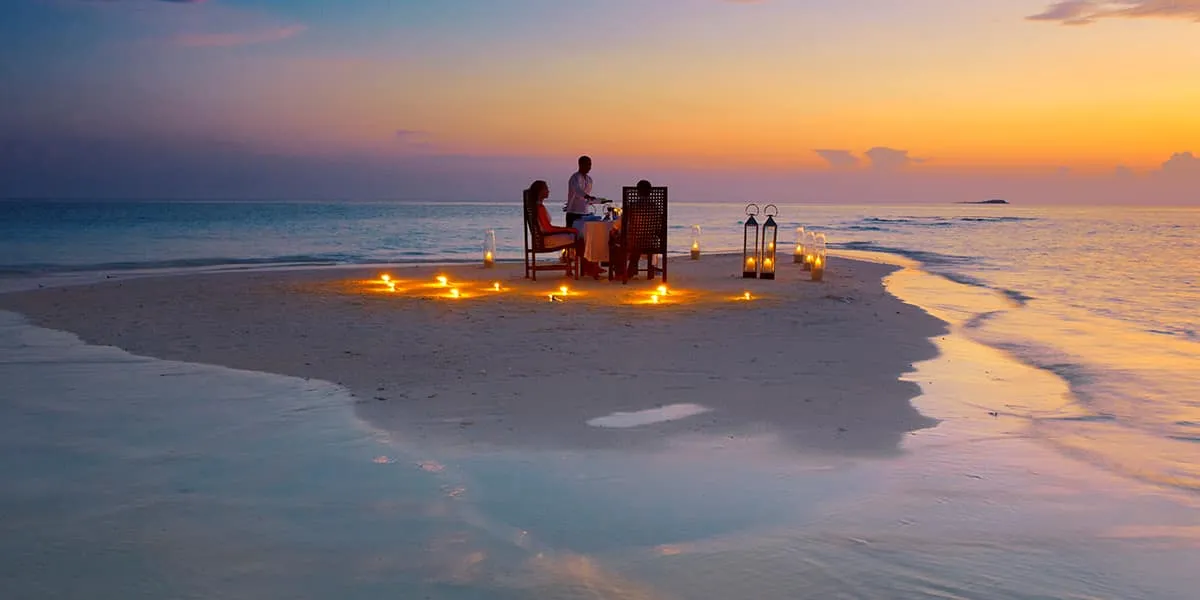 Couple dining at a candlelit table on a sandbank at dusk