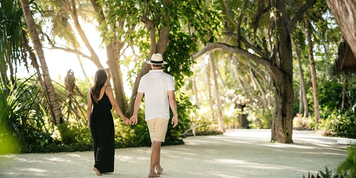 Couple walking hand in hand along a sandy path under tall trees