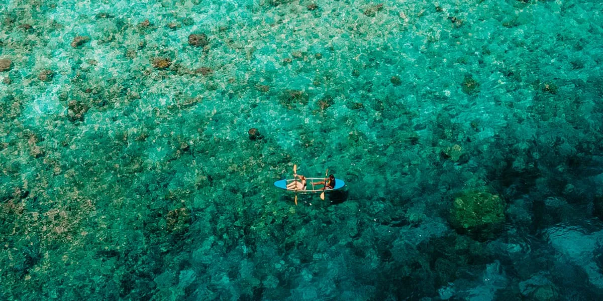 Aerial view of a kayaker paddling over a green-blue reef
