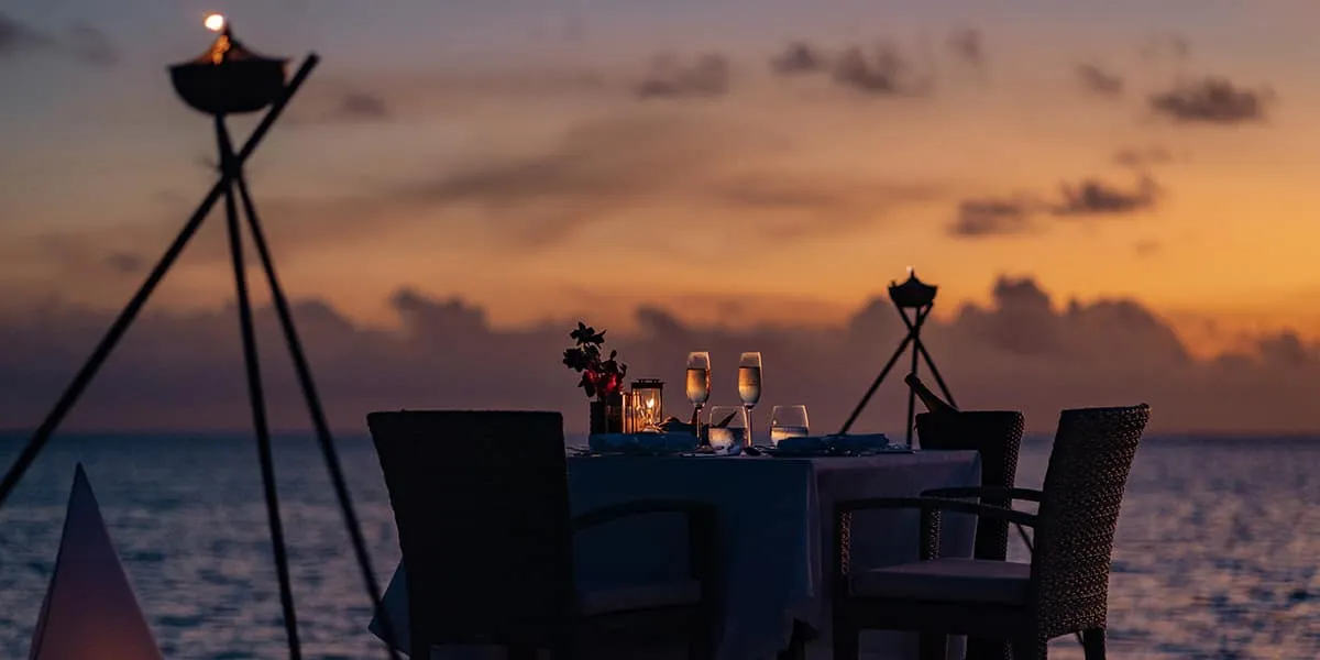 Table set for two on a deck at sunset beside lit torches