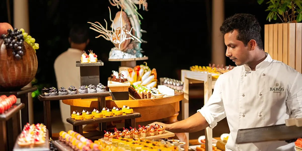 Chef in whites beside a festive dessert buffet at night
