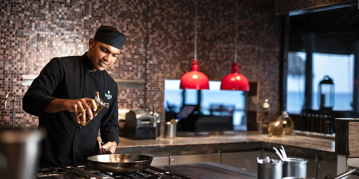Chef in black cooking at the stove in an open kitchen