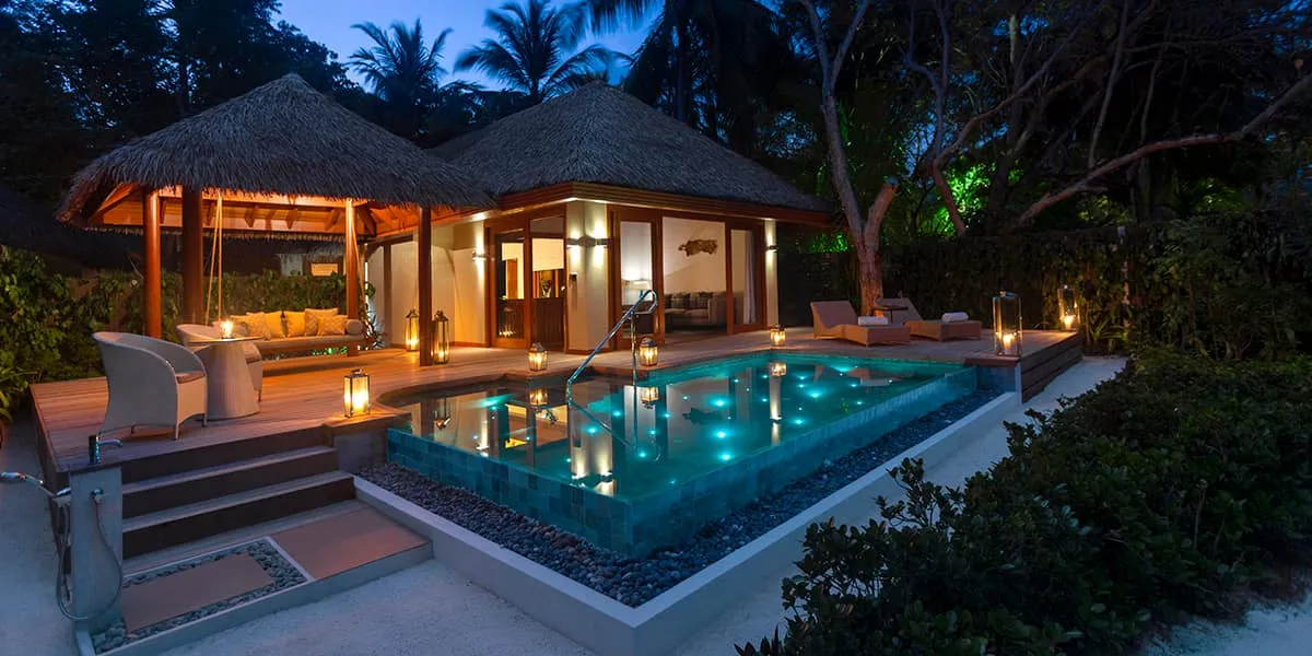 Baros Suite with a lit private pool and thatched pavilions at twilight