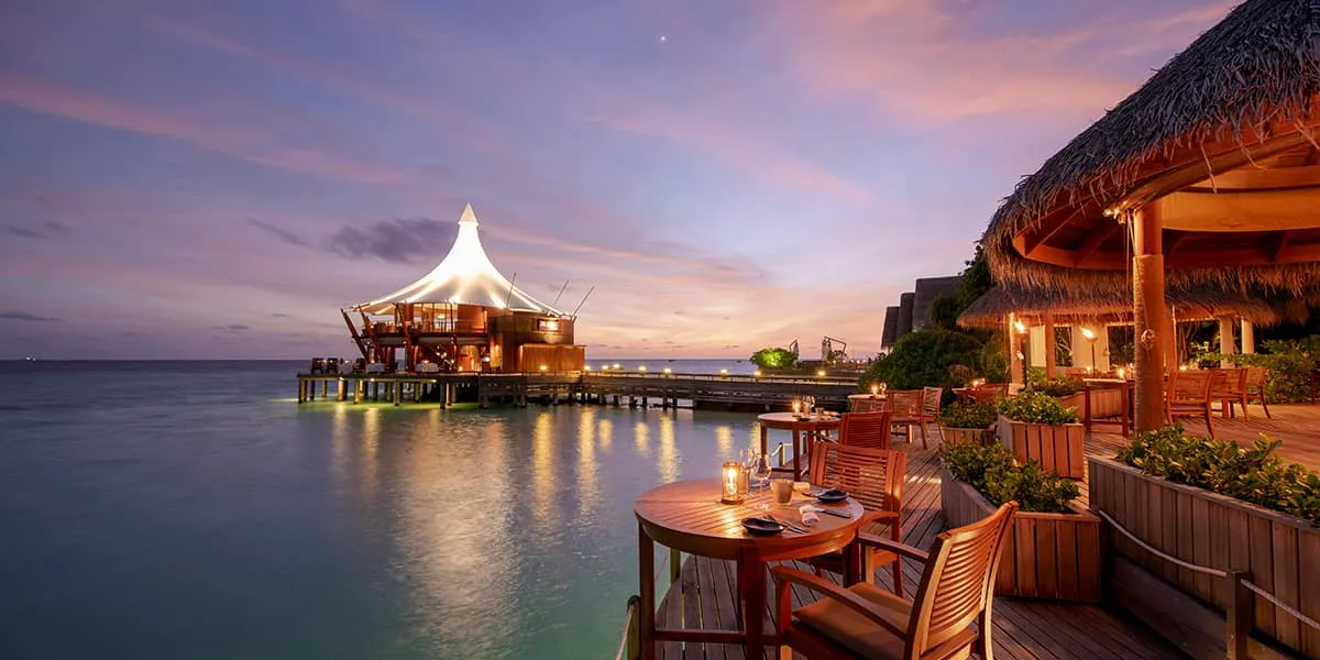 Candlelit Cayenne Grill terrace over the lagoon at dusk, the Lighthouse beyond