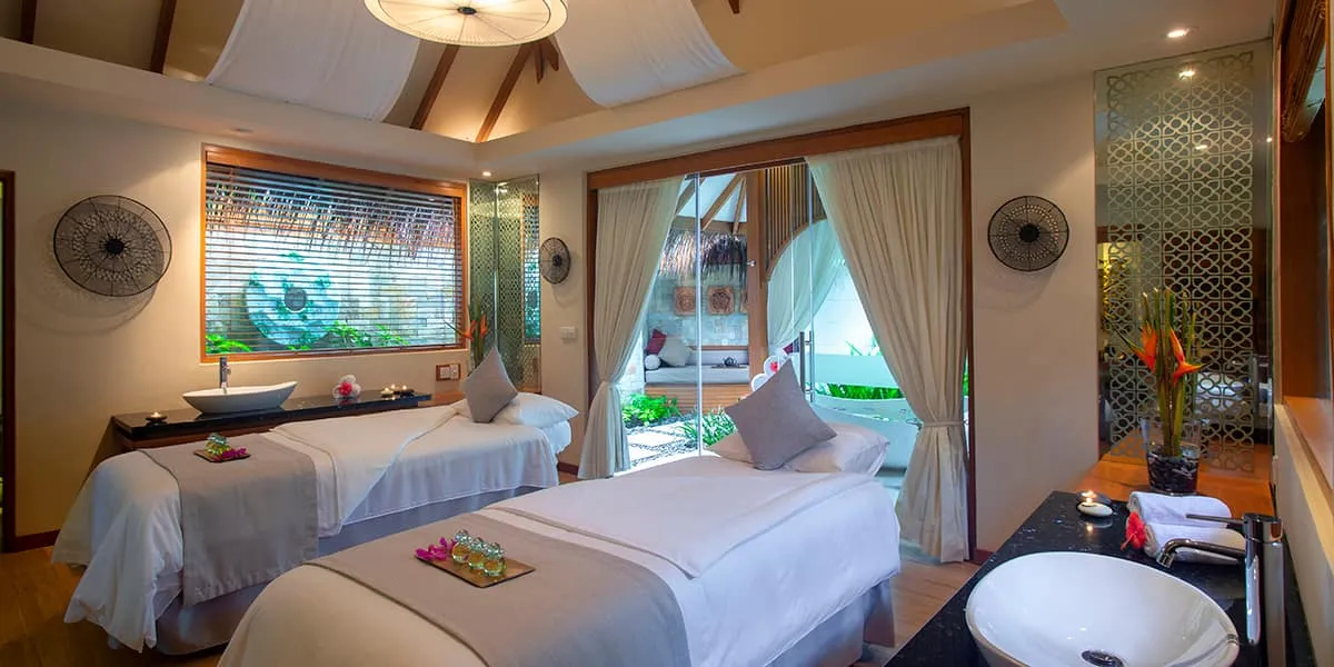 Spa treatment room with two massage beds, a basin and garden views
