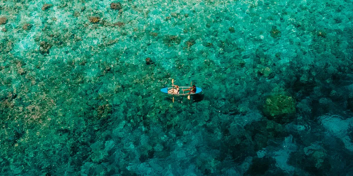 Aerial view of a kayaker paddling over a green-blue reef