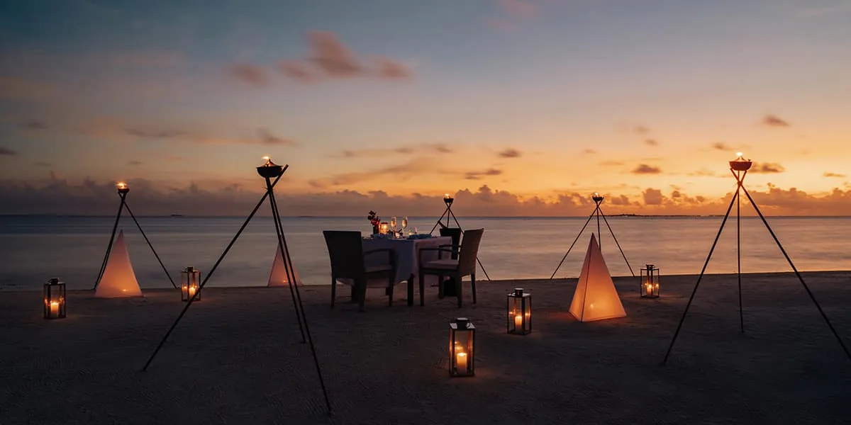 Table for two on the beach at dusk, lit by lanterns and tripod torches