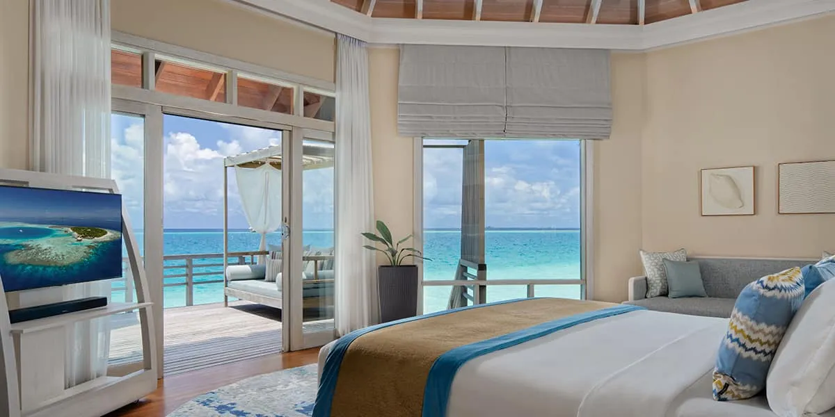 Water villa bedroom with glass doors opening onto a sea-view deck