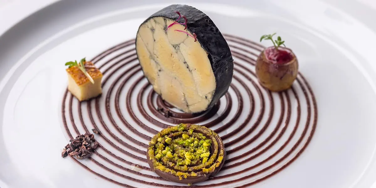 Plated dessert with a chocolate spiral, pistachio tart and garnishes