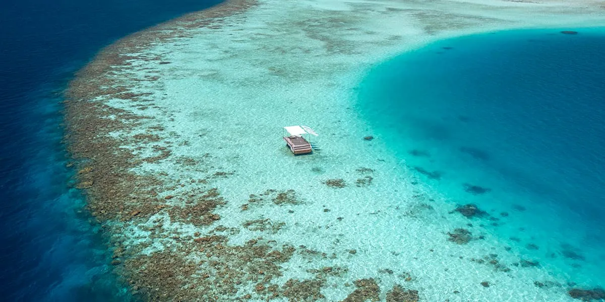 Aerial view of a boat in a turquoise lagoon beside the reef edge