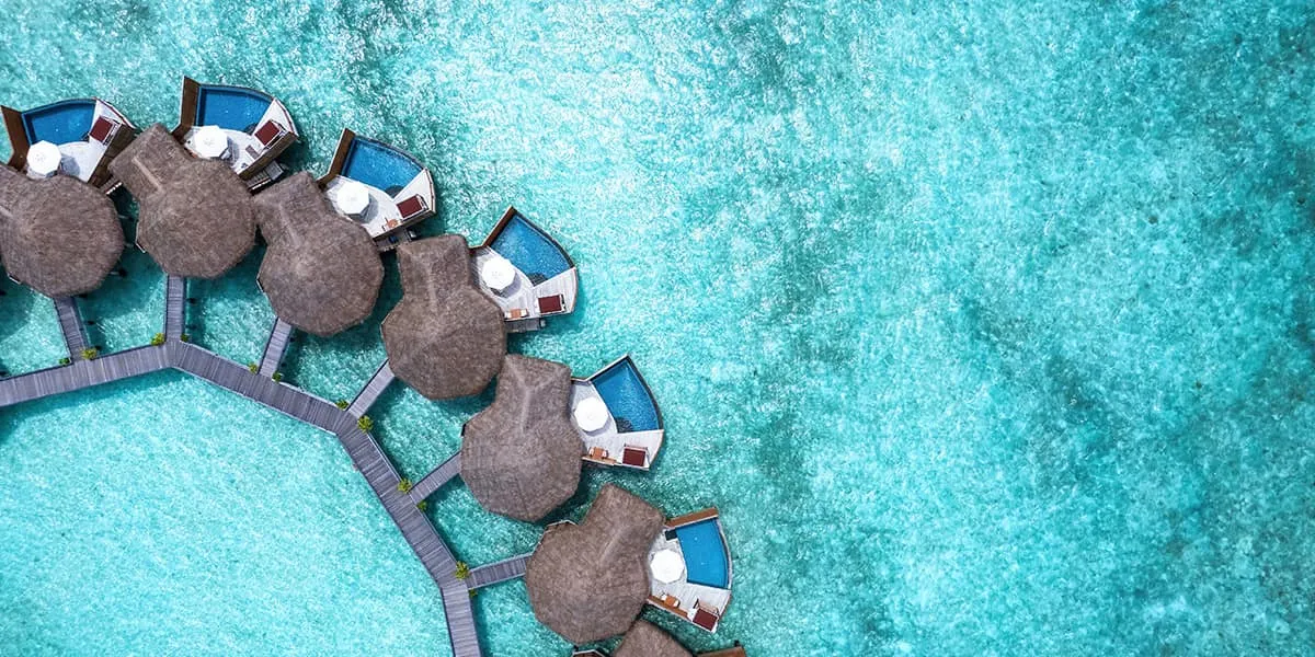 Aerial view of thatched water villas curving over a turquoise lagoon