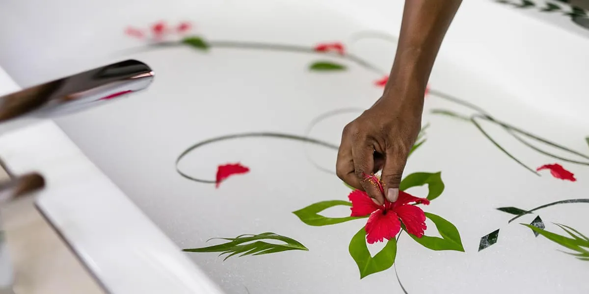 Hand arranging red flowers and green leaves into a pattern on a white bed