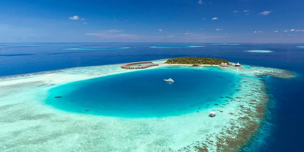 Aerial view of Baros island beside a deep blue lagoon ringed by reef