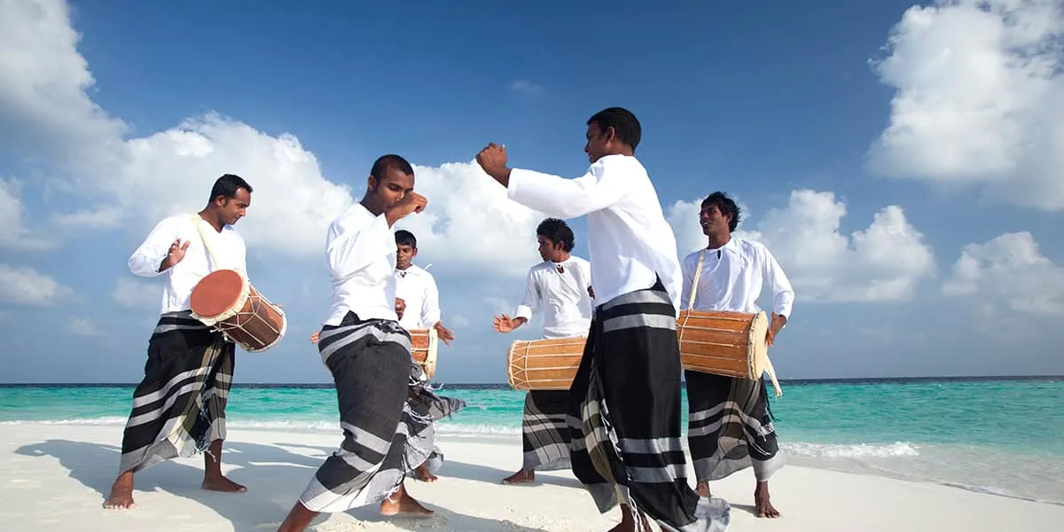Bodu beru drummers in white shirts and sarongs performing on a sandbank