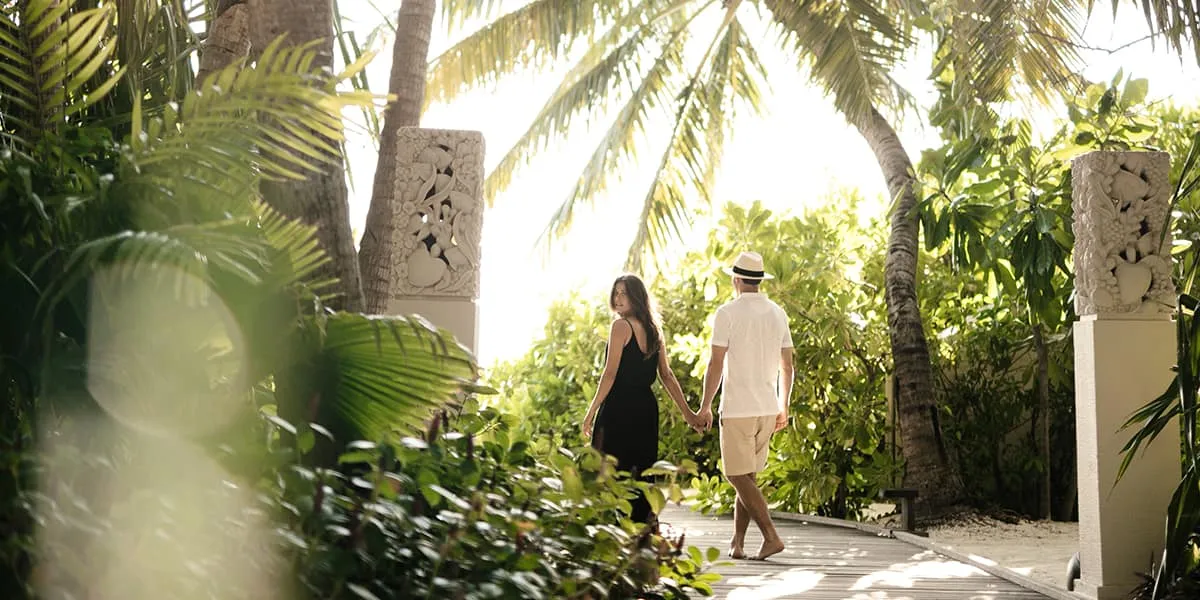 Couple walking along a sunlit garden path between carved stone pillars