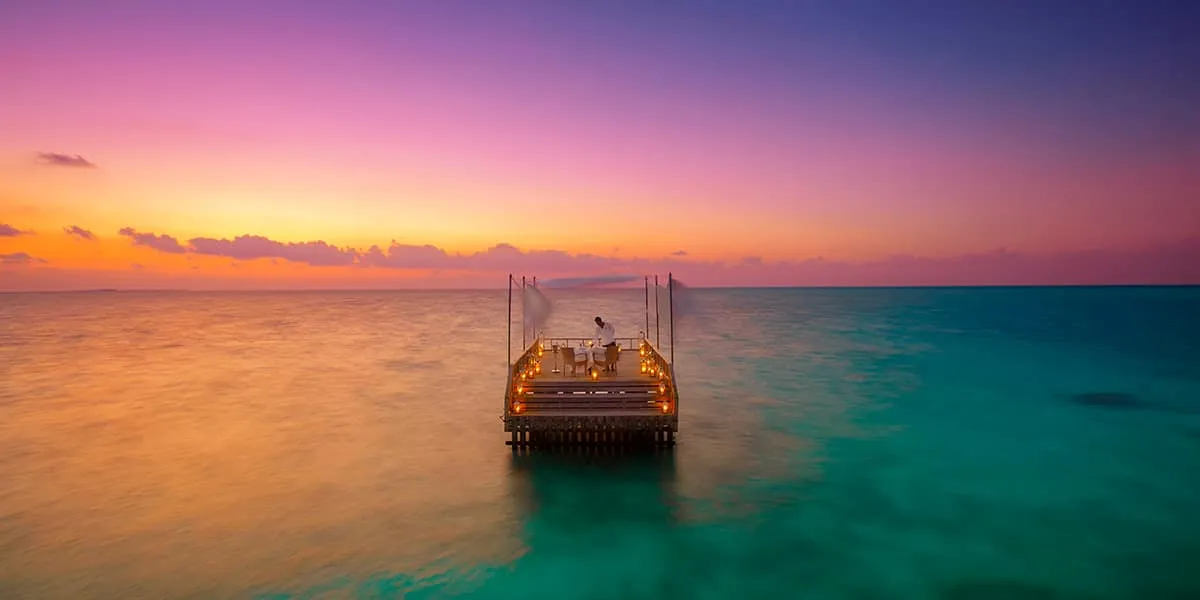 Candlelit piano deck in the lagoon under a pink and orange sunset sky