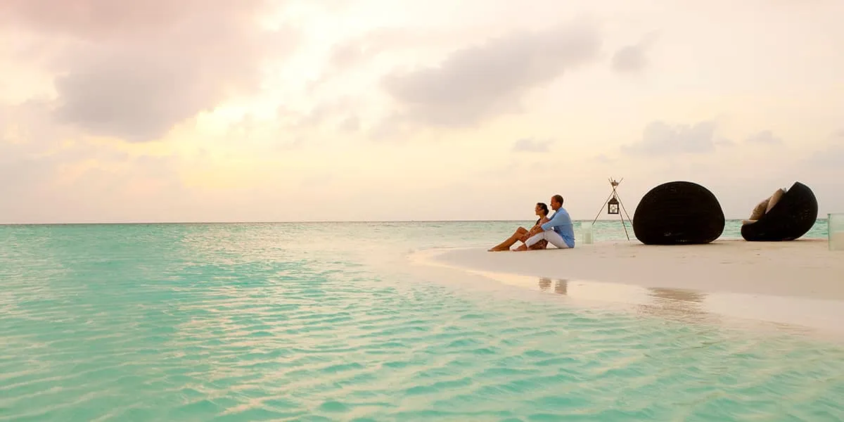 Couple sitting at the water's edge on a sandbank beside large beanbags