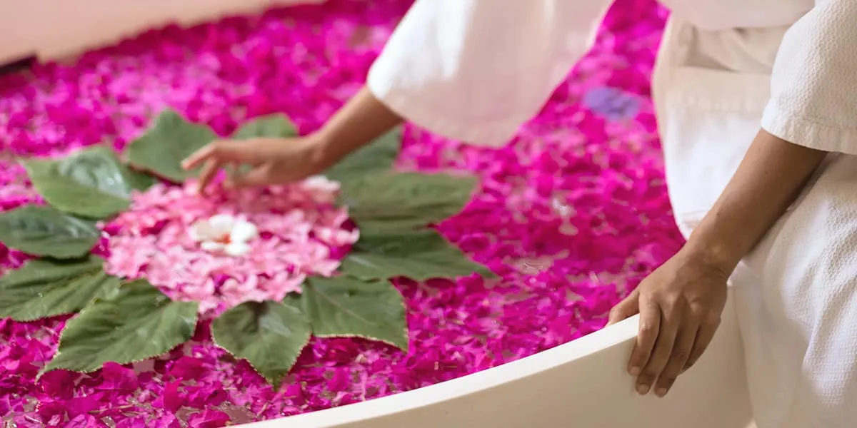 Hand arranging flowers on a petal-filled spa bath