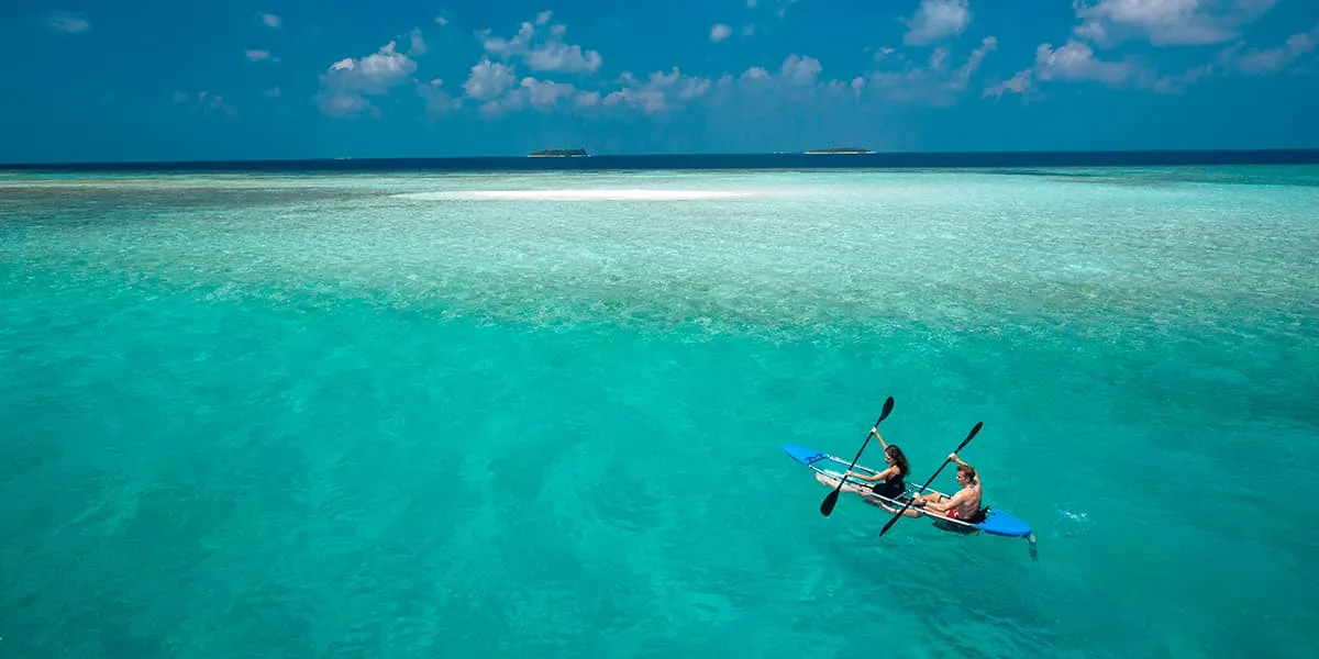 Couple paddling a transparent kayak across a turquoise lagoon