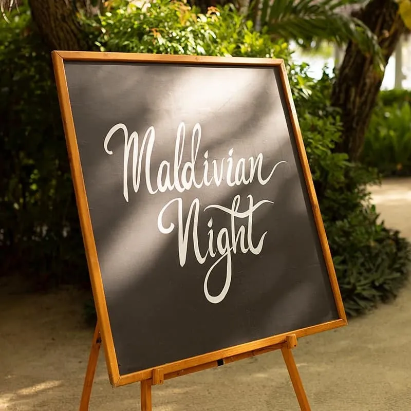 Chalkboard sign reading "Maldivian Night" on an easel in a garden