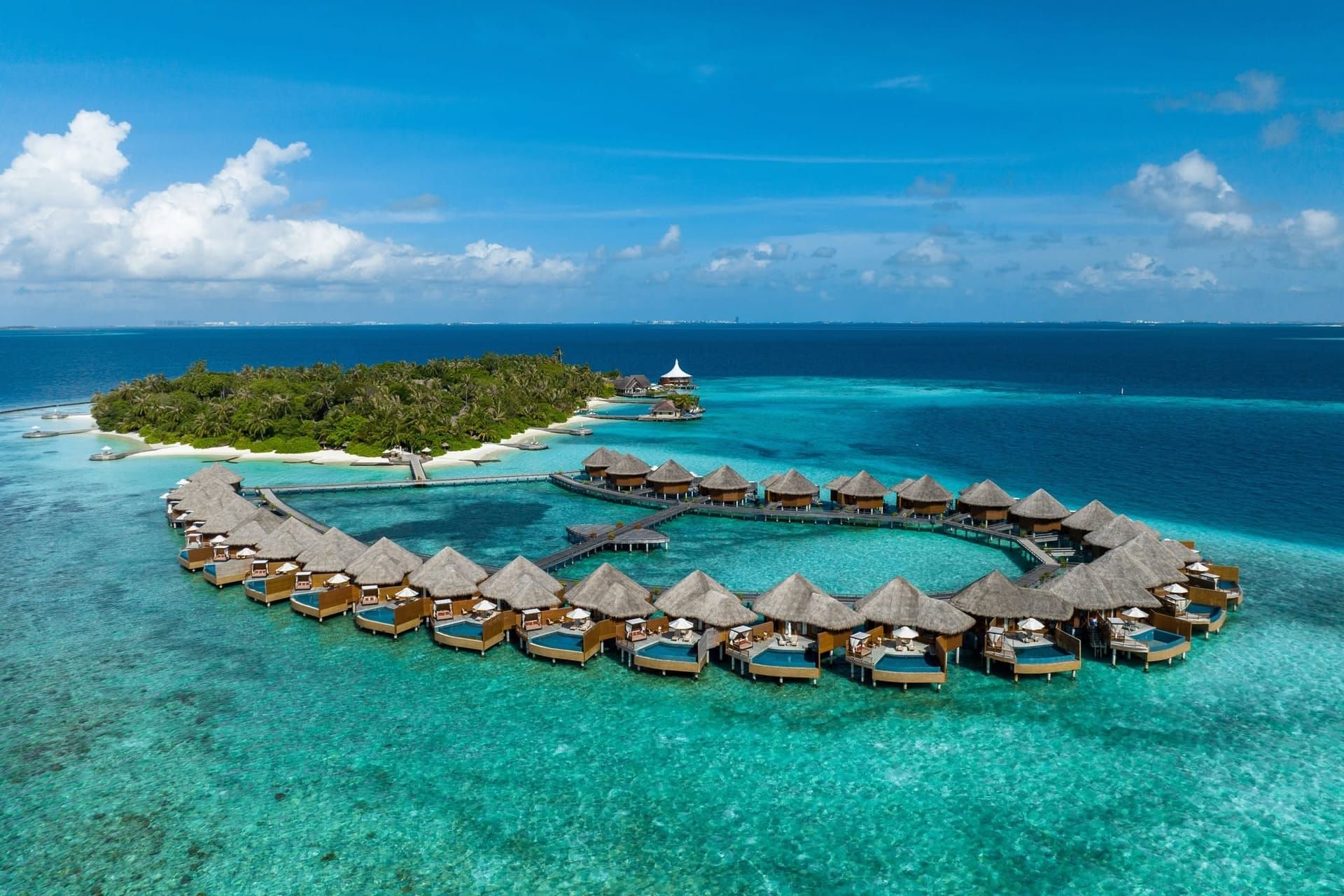 Aerial view of Baros island and its ring of overwater villas under a blue sky