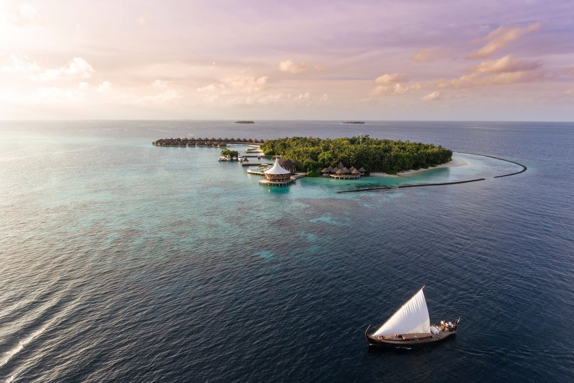 Baros island at dawn seen from the sea, with a traditional dhoni sailing in the foreground