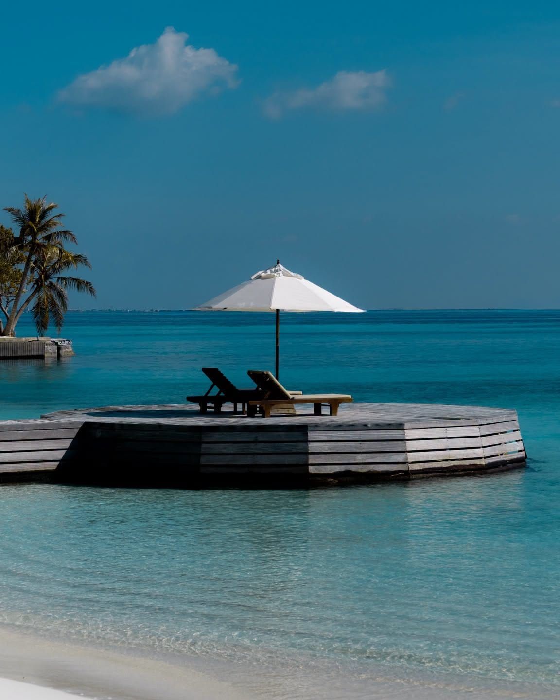 Circular overwater deck with parasol and loungers in a calm turquoise lagoon