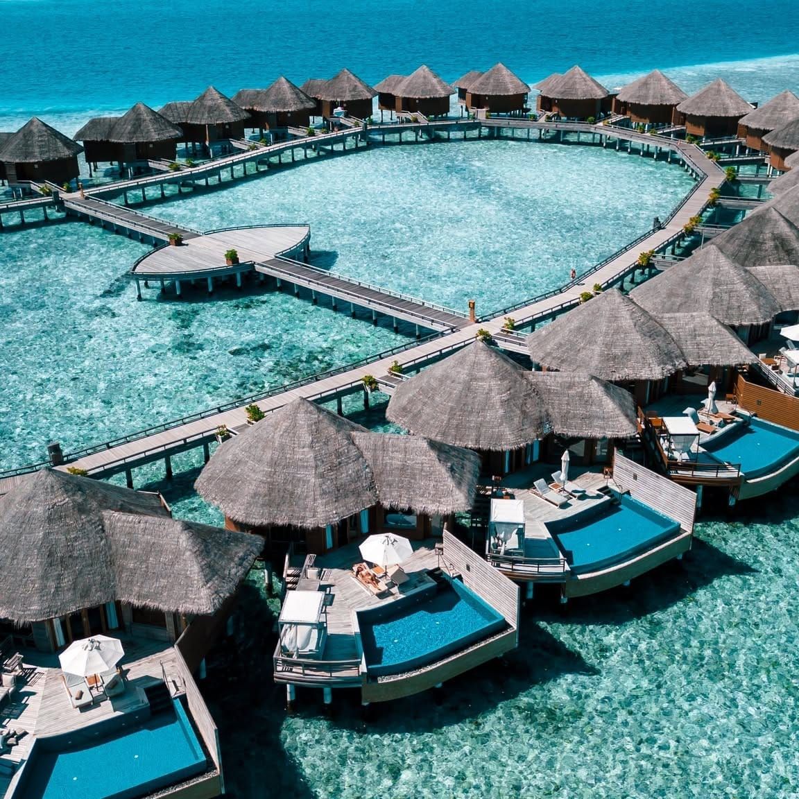 Aerial view of overwater villas with private pools along a curving boardwalk