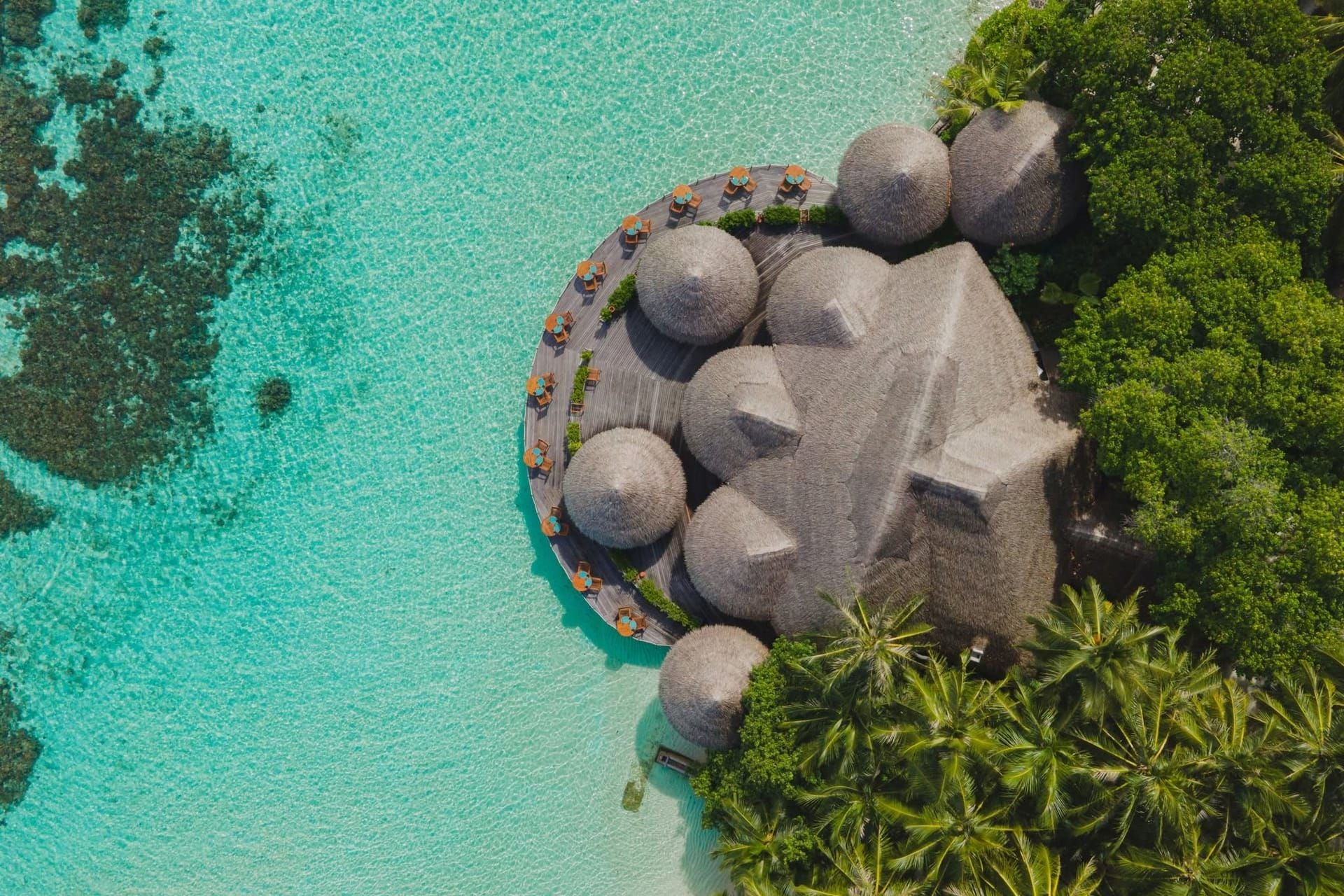 Aerial view of a thatched domed pavilion on the shoreline above a turquoise lagoon