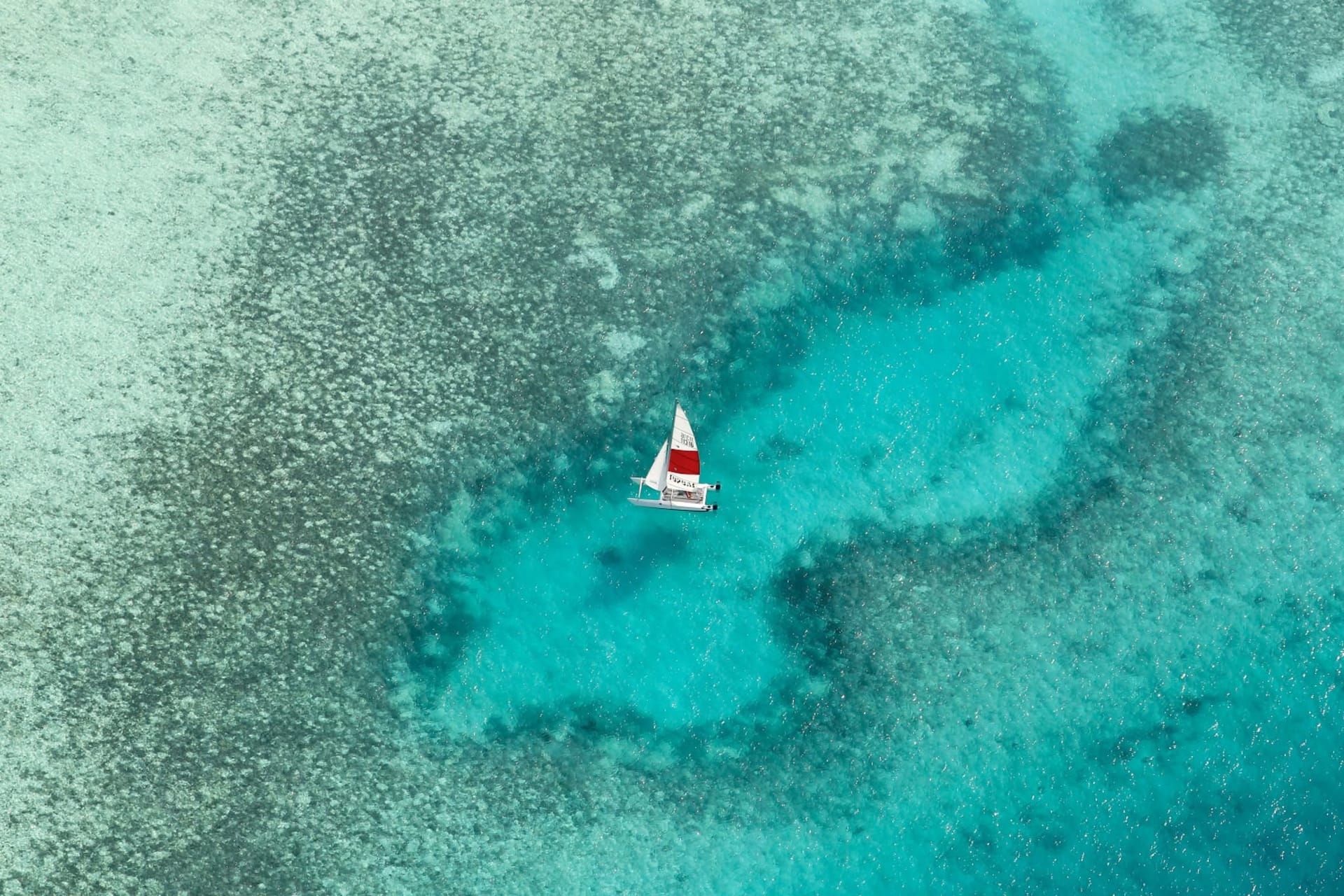 Aerial view of a small sailboat crossing a turquoise reef lagoon