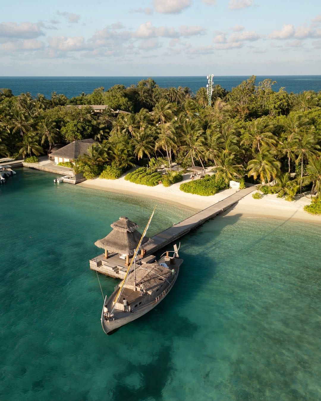Aerial view of a moored wooden boat by a jetty off a palm-fringed island beach