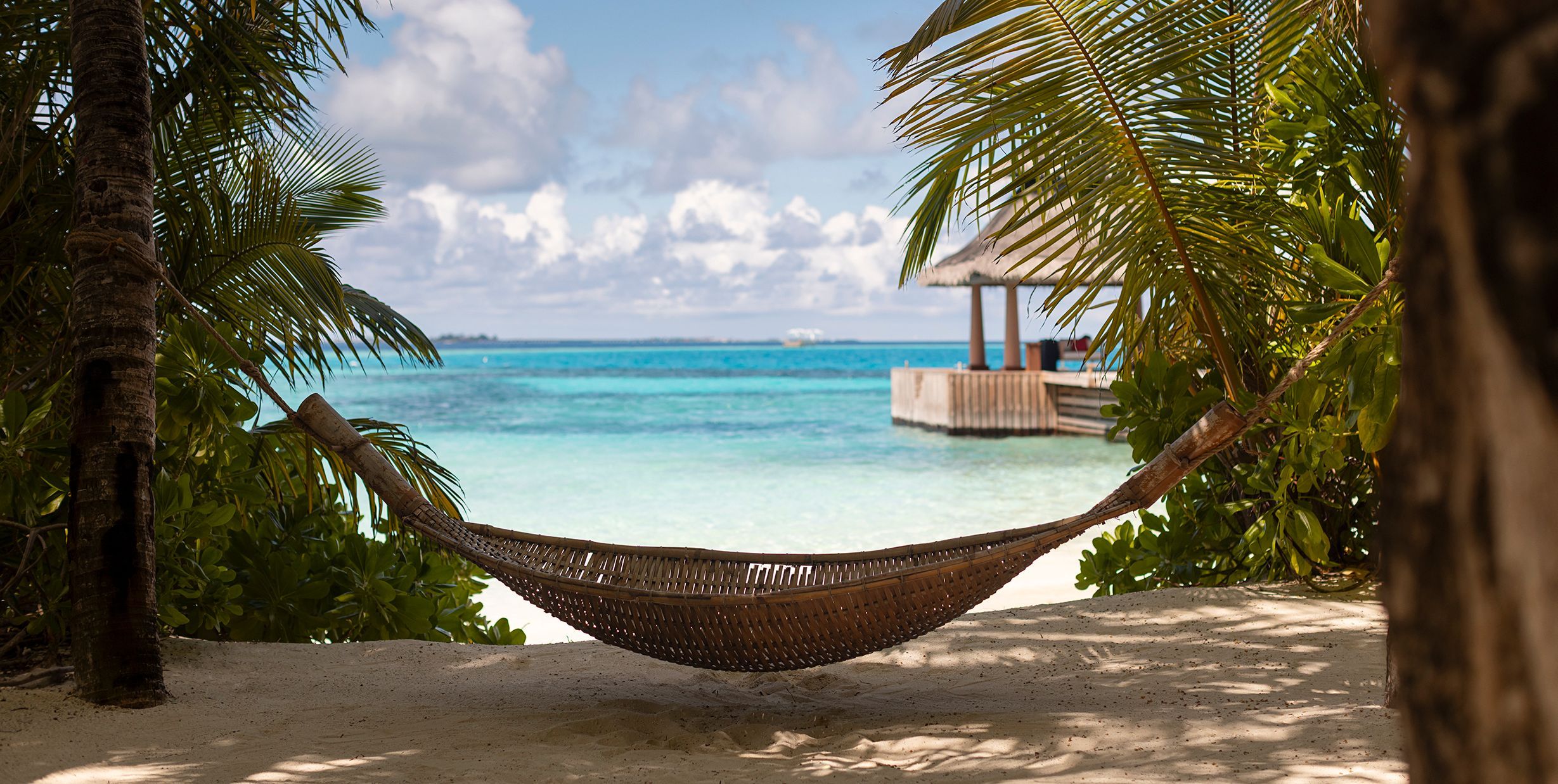 A hammock between palm trees on a white-sand beach, looking out to the turquoise lagoon