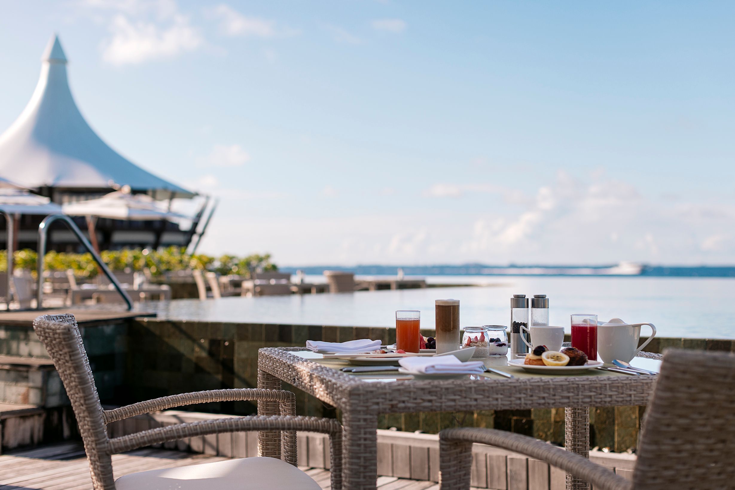 A breakfast table set with juices and plates by the infinity pool at Lime, with the Lighthouse in the background