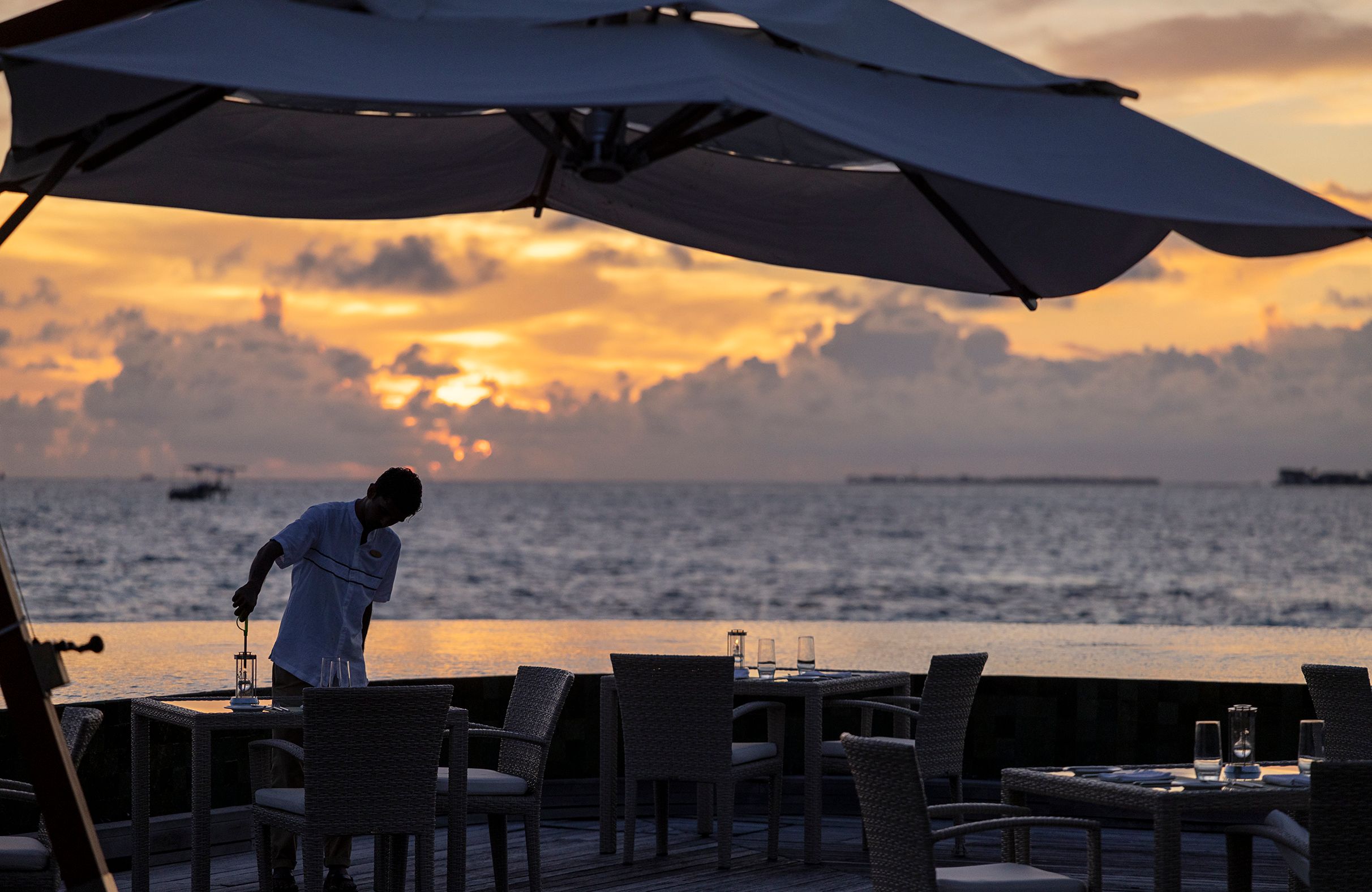 A waiter preparing a table on the Lime pool deck at sunset