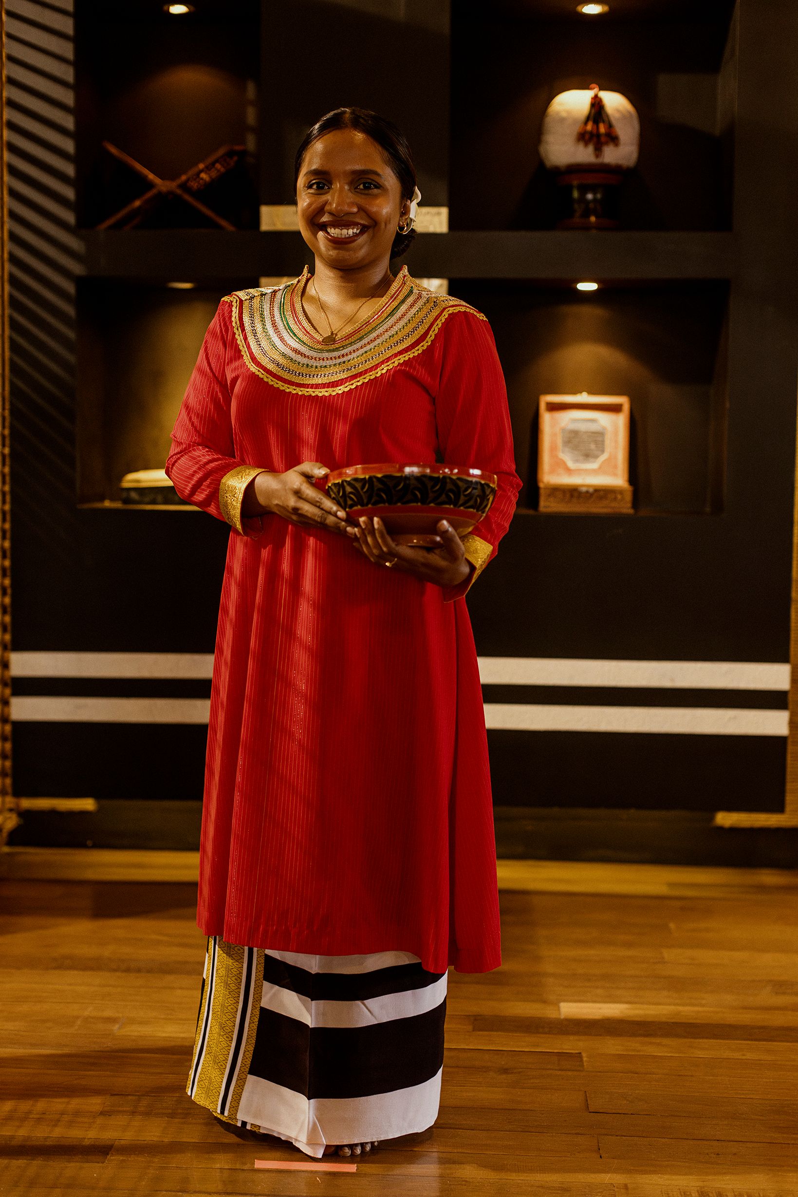 A Baros team member in a red Maldivian dress holding a woven basket in the Maldivian Lounge