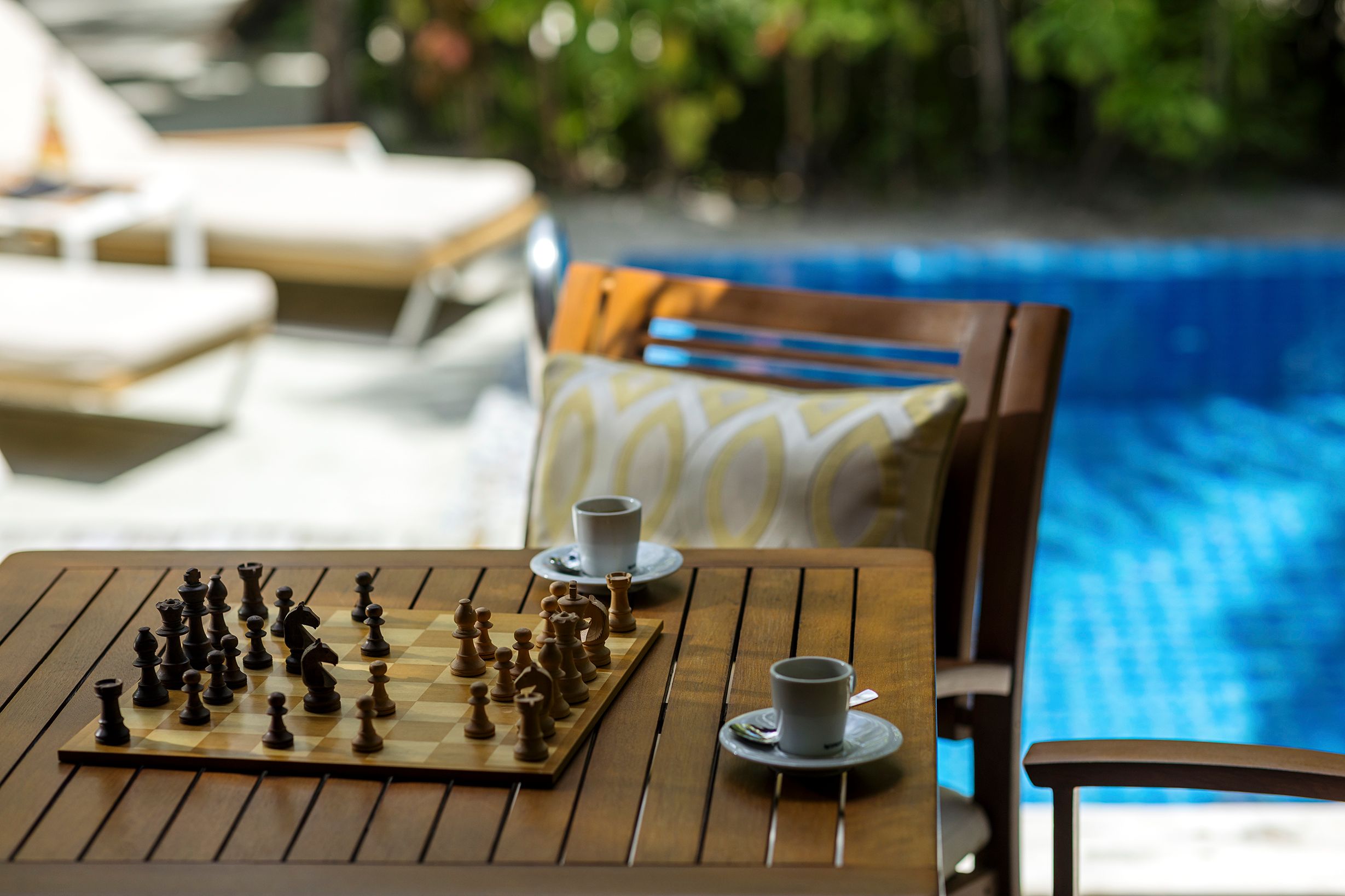 A chessboard and coffee cups on a table beside a Pool Villa pool